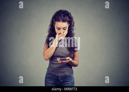 Junge begeistert Mädchen für Mund und Lesen von Nachrichten auf dem Smartphone in starke Reaktion auf grauem Hintergrund. Stockfoto