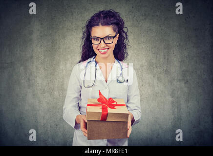 Hübsche Brünette in weißem Kleid von medizinischen, verpackt in Geschenkbox Kamera lächelnd auf Grau. Stockfoto