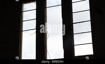 Gebrochene Fenster in einem verlassenen Gebäude - Ansicht von innen - Himmel mit Wolken durch das Fenster gesehen. Stockfoto
