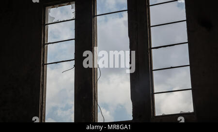 Gebrochene Fenster in einem verlassenen Gebäude - Ansicht von innen - Himmel mit Wolken durch das Fenster gesehen. Stockfoto