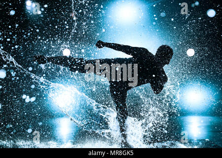 Junger Mann pause Tanzen im Club mit Licht und Wasser. Blau getönten Farben und dramatische Silhouette. Stockfoto
