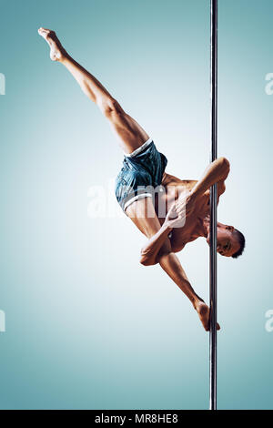 Junge starke Mann Pole Dancing auf blauem und weißem Hintergrund Stockfoto