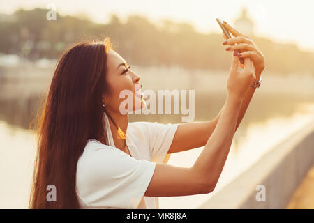 Junge asiatische Frau tun selfie auf city river Hintergrund am sonnigen Morgen Stockfoto