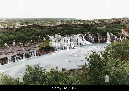 Majestätische Landschaft mit Wasserfällen Hraunfossar und grüne Vegetation auf Hügeln in Island Stockfoto