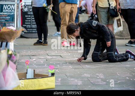 Ein junges Mädchen schreibt Nachrichten in Kreide auf dem Bürgersteig in St. Ann's Platz, der vor dem Manchester zusammen Konzert im Gedenken an die Opfer der Arena Bombenattentat in Manchester, Großbritannien, am 22. Mai 2018. Prinz William und der britische Premierminister Theresa May zusammen mit anderen Politikern, sowie Angehörige der Getöteten, und Rettungskräfte zur Szene des Terror Angriff, während Tausende von Menschen in Manchester Dienstag versammelten sich am ersten Jahrestag des Terrorangriffs in der Stadt die 22 Toten. Stockfoto