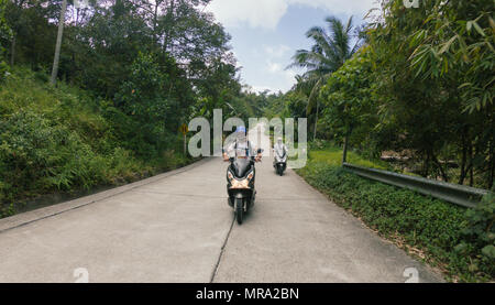 Mann fahren Fahrrad Roller auf der Straße mit Palmen in Thailand Stockfoto
