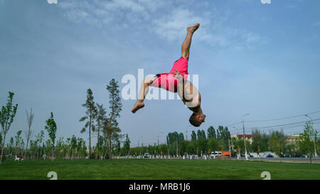 Austrickst, auf Rasen im Park. Der Mensch macht zurück und Kick. Kampfkunst und Parkour. Street Workout. Stockfoto