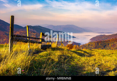 Schönen bergigen Landschaft mit Holzzaun. schöne herbstliche Landschaft bei Sonnenaufgang mit herrlichen Himmel über dem Tal voller Nebel Stockfoto