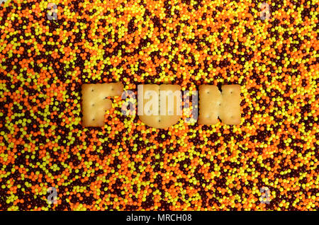 Spaß. Das Wort von den essbaren cracker Buchstaben liegt auf der verglasten Pulver. Eine große Anzahl von süßen, bunten Perlen von sehr kleinen Größe für die Dekoration von Stockfoto