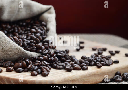 Einen vollen Beutel der braunen Bohnen liegt auf einem Holz- Oberfläche. Attribute, die mit der Zubereitung von Kaffee im Zusammenhang Stockfoto