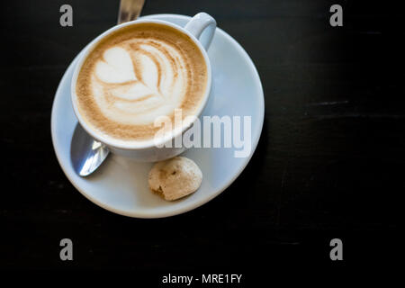Cappuchino oder latte Kaffee in eine weiße Tasse mit herzförmigen Schaum auf Holzbrett. Morgen energy dring auf dunklem Hintergrund. Kopieren Sie Platz. Ansicht von oben Stockfoto