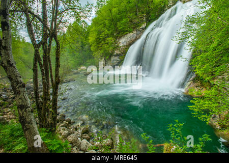 Schönen Wasserfall, abgeschieden im Wald, umgeben von grünen Bäumen, von Felsen gesäumt, bilden ein Türkis Teich von Wasser an der Basis. Stockfoto