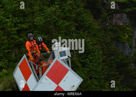 Besatzungsmitglieder der Küstenwache Aids zur Navigation Team Sitka erwarten von einem Coast Guard Air Station Sitka MH-60 Jayhawk Helikopter Crew nach Abschluss der Wartung für die Kap Edgecumbe Licht auf einem Felsen in einer Höhe von etwa 150 Metern in einem Regenwald auf Kruzof Island in Sitka, Alaska, 7. Juni 2017 gehisst entfernt werden. Etwa die Hälfte der ANT Sitka 112 Aids zur Navigation erfordern die Bereitstellung von Personal mit dem Helikopter Besatzungen das Licht zu warten. U.S. Coast Guard Foto von Petty Officer 1st Class Bill Colclough. Stockfoto