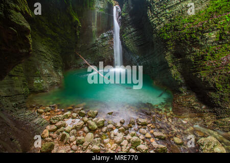 Versteckten Wasserfall Kozjak streams aus geschichteten, bemoosten Felsen in eine tiefe Schlucht. blaues Wasser, geisteskrank glasklaren Pool, Felsen und toter Baum. Lange Belichtung. Stockfoto