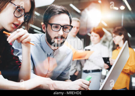 Moderne bärtigen Geschäftsmann und seine Kollegen, ein Mädchen in Gläsern, mit der Arbeit an einem neuen Projekt hinter einem Laptop. Entwickeln und einen neuen Anlauf zu diskutieren developme Stockfoto