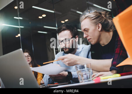 Team von jungen Studenten arbeitet an einem neuen Projekt, diskutieren Diagramme auf Papier und Laptop in einem modernen Loft Raum Stockfoto