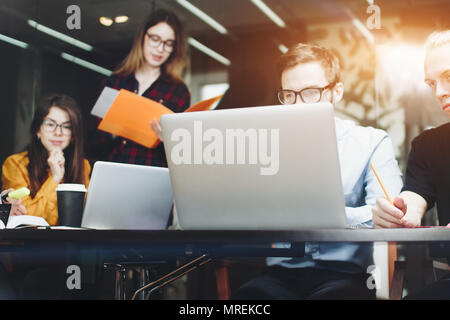 Team von Designern sitzt an einem hölzernen Tisch in einem modernen Büro und arbeitet auf Laptops. Unternehmen der Kollegen diskutiert über Neue stratup Stockfoto
