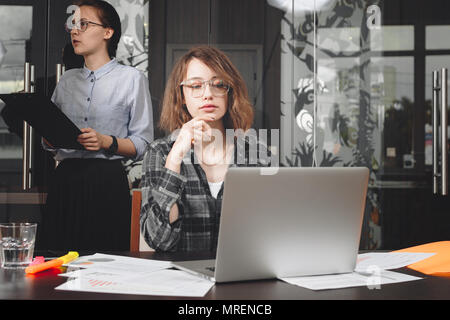 Junge Geschäftsfrau in Gläsern arbeiten an modernen Laptop im Loft Büro. Foto von nachdenklich weibliche Manager oder Architekten arbeiten an neuen Projekt Stockfoto
