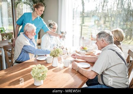 Die Frau Arbeitnehmer ältere Erwachsene am Tisch in der Pflege zu Hause. Stockfoto