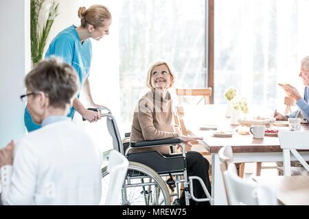 Ältere Frau im Rollstuhl in Richtung care Worker lächelnd. Stockfoto
