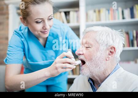 Care worker helfen älteren Mann mit Inhalator. Stockfoto