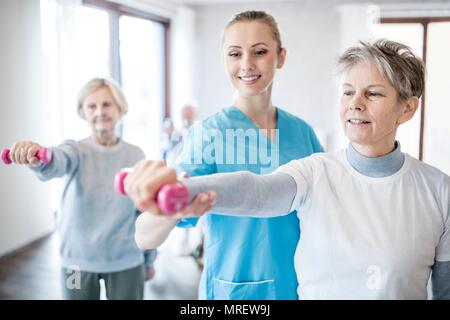 Ältere Frau die Hand Gewicht, Physiotherapeut hilft. Stockfoto