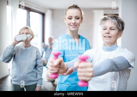 Senior woman holding Trainingshanteln, Physiotherapeut hilft. Stockfoto