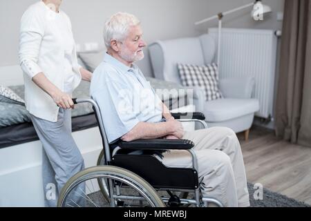 Älterer Mann im Rollstuhl mit Frau in der Pflege zu Hause. Stockfoto