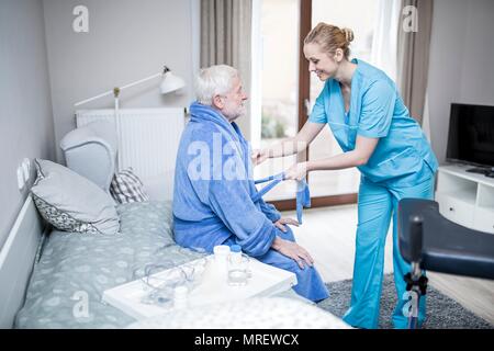 Care worker helfen älteren Menschen auf Morgenmantel zu setzen. Stockfoto