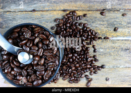 Fokus auf gerösteten Kaffeebohnen in einer kaffeemühle von Hand. Und geröstete Kaffeebohnen auf Holz- Hintergrund. Stockfoto