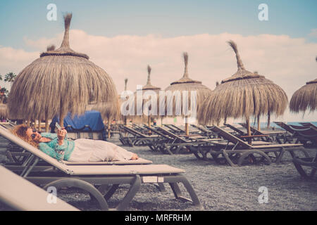Schönen kaukasischen Frauen mittleren Alters auf die Sitze legen am Strand mit tropischen Sonnenschirme. Reisen und Ferien rest Konzept. Bleiben Sie verbunden wit Stockfoto