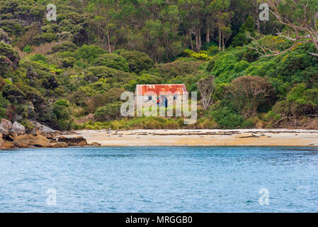 Stewart Island, Neuseeland - 22. Februar 2018. Eine Gruppe von vier Personen steht vor einem kleinen Steinhaus in einem Wald auf Stewart Island. Redaktionelle Verwendung Stockfoto