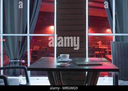 Eine Tabelle in der Nacht Cafe mit einem Becher aus Kaffee und das Konto vor dem Hintergrund eines Fensters Stockfoto