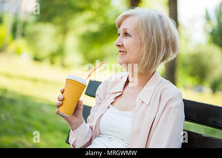 Glückliche erwachsene Frau sitzt im Park und Kaffee zu trinken. Stockfoto