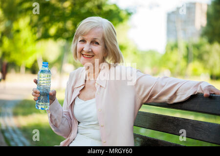 Erwachsene Frau sitzt im Park und Trinkwasser. Stockfoto