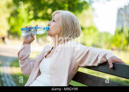 Erwachsene Frau sitzt im Park und Trinkwasser. Stockfoto