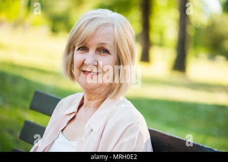Glückliche erwachsene Frau sitzt im Park und ihre Zeit genießen. Stockfoto