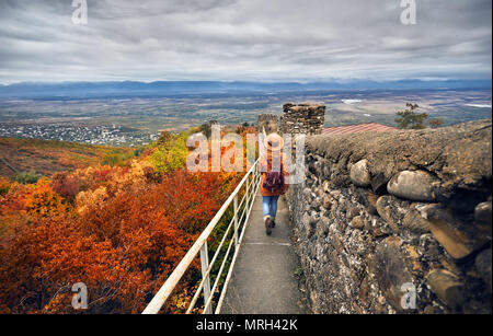 Touristische Frau in braunen Hut und Rucksack zu Fuß auf der alten Stadtmauer mit Blick auf Alasani Valley im Herbst mal in Signagi, Georgien