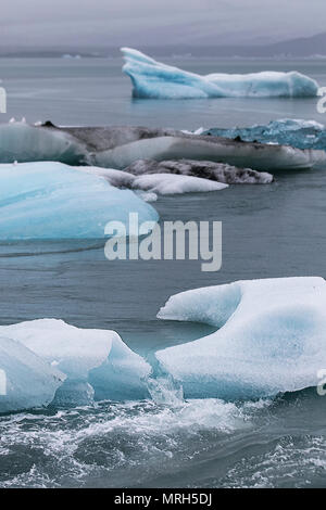 Eisschollen an der Jokulsarlon Gletscherlagune bei Breiðamerkurjökull, einem Auslaufgletscher des herrlichen Vatnajökull Gletschers, der dahinter liegt. Eisscholle, Eisschwimmen, Meereis, Drift-Eis, blaues Eis Eisscholle, Meereisbildung und -Merkmale, schwimmende Eisblöcke, Flöße und Hummocks, eine große Packung schwimmenden Eises am Diamond Beach. Der Jokulsarlon Gletscher, treiben, schwimmen, schmelzen, Erwärmung, polar, arktisch, global, Gletscher, blau, kalt, tauen Landschaft, Ozean Lagune schwarzen Sandstrand, Island. Stockfoto