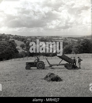 1950er Jahre, historische Ansicht der Landwirtschaft in den Cotswolds, Gloucestershire, England, UK, einem männlichen Landwirt auf seinem Traktor mit Landarbeitern entladen Futter oder Futtermittel auf das Gras Feld aus dem Trailer. Stockfoto