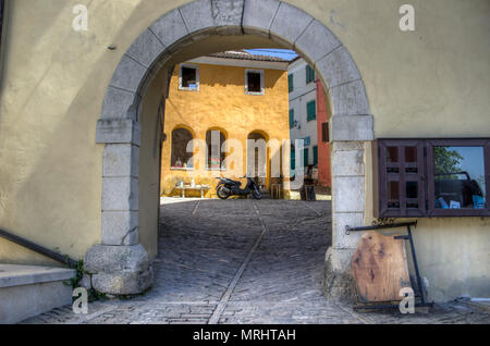 Istrien, Kroatien, April 2018 - Blick durch einen Torbogen auf einen Roller vor einem alten gelben Haus in der Altstadt von Oprtalj geparkt Stockfoto