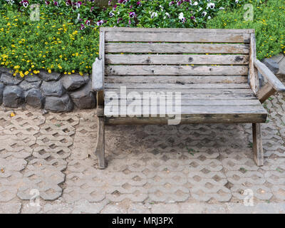 Bank aus Holz auf dem Backstein, in der Nähe des Beetes im öffentlichen Park. Stockfoto