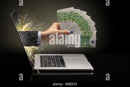 Hand mit Geld aus einem Laptop mit funkelnden Effekten Stockfoto