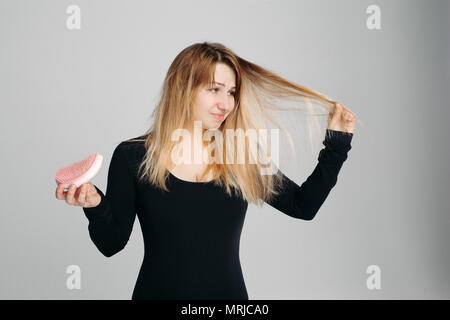 Pretty Woman Holding unordentlichen Haar in einer Hand und Haarbürste in ein anderes. Stockfoto