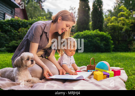 Junge Mutter mit Kind und Hund sitzt im Park und lesen Buch Stockfoto