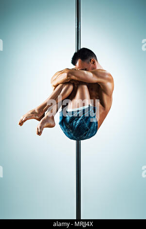 Junge starke Mann Pole Dancing auf blauem und weißem Hintergrund Stockfoto