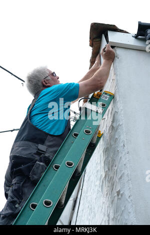 Ein Builder arbeiten auf einer Leiter die Regenrinne eines Hauses zu reparieren. Stockfoto