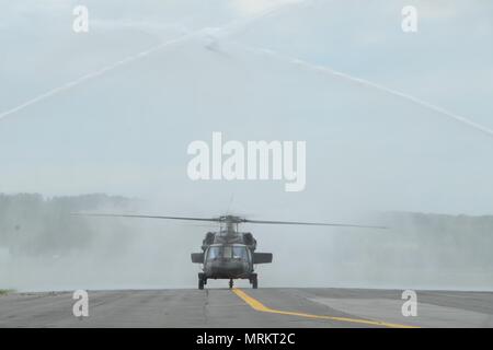 Der Sikorsky UH-60 Black Hawk ist ein Nutzhubschrauber der US Army, der für den taktischen Transport und die Unterstützung entwickelt wurde. Er wird von zwei Turbowellenmotoren angetrieben und mit einem vierblättrigen Hauptrotor ausgestattet. Das Archivbild erfasst das Flugzeug, das sich während einer letzten Flugzeremonie im Juni 2017 durch einen von Flughafenfeuerwehrfahrzeugen erzeugten Wasserbogen nähert. Stockfoto