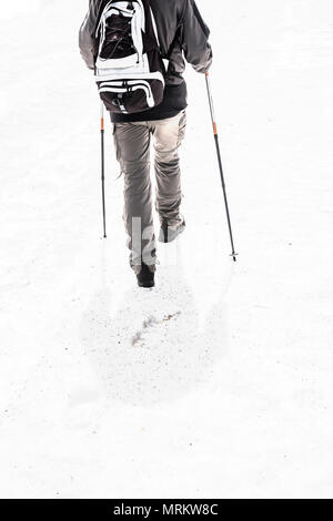 Mann in den Bergen unterwegs mit Schnee mit Wanderausrüstung, Bergschuhe und Stöcke Stöcke. Überleben Konzept. Farbe Wirkung. Stockfoto