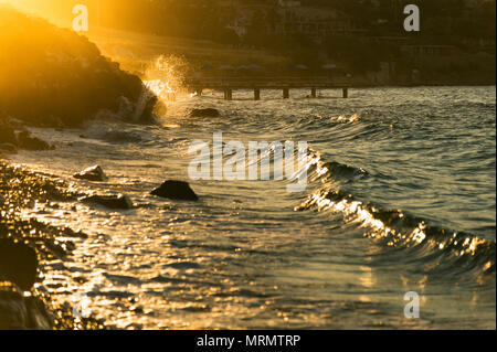 Steiniger Strand mit Wellen und mit goldfarbenen Sonne leuchtet am Abend. Stockfoto